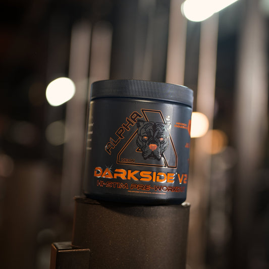A black tub of Alpha Neon Darkside V2 pre-workout supplement, displayed on a gym machine with a blurred gym background.