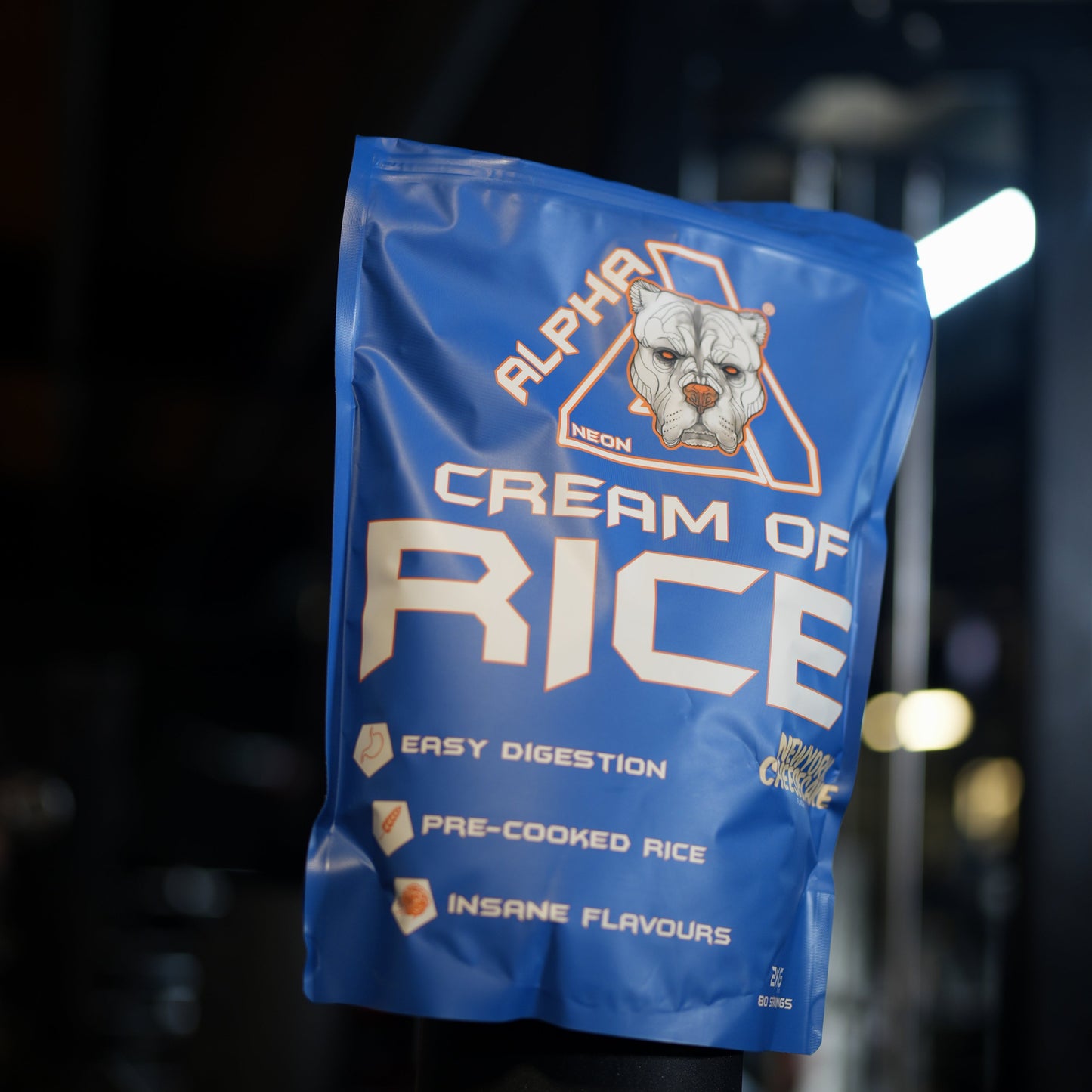 A blue stand-up pouch of Alpha Neon Cream of Rice pre-cooked rice, photographed hanging against a dark, blurred background with bright lights.