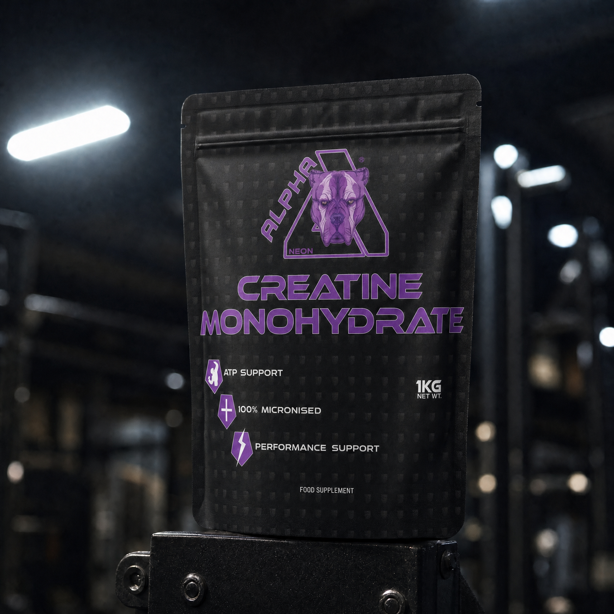 A black stand-up pouch of Alpha Neon Creatine Monohydrate supplement, featuring purple text and a purple dog logo, photographed in a gym setting with blurred equipment and lights in the background.