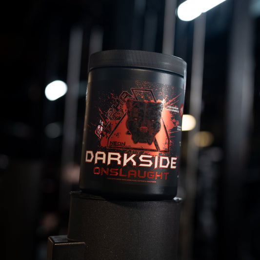 A black tub of Darkside Onslaught pre-workout powder standing on a black stand in a dark gym environment with blurred lights in the background.