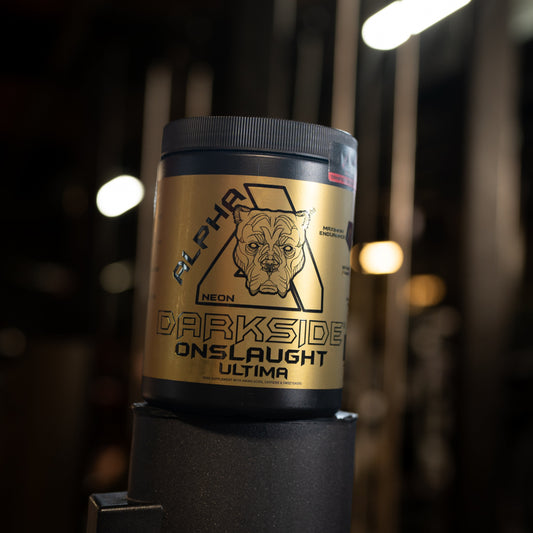 A black tub of Alpha Neon Darkside Onslaught Ultima supplement powder with a metallic gold label, set against a dark gym background with blurred lights.