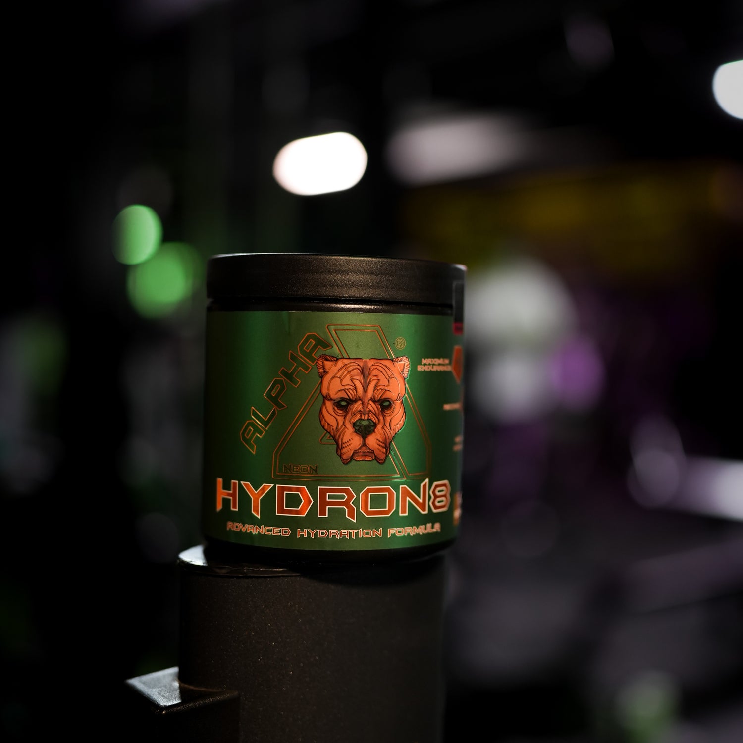 A green tub of Alpha Neon Hydron8 Advanced Hydration Formula with a black lid, featuring a graphic of a dog's face on the label, set against a dark, blurred background with bokeh lights.