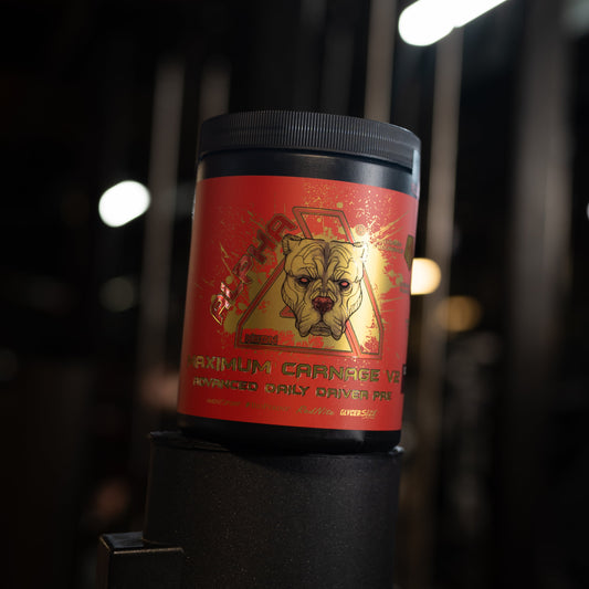 A red tub of 'Maximum Carnage V2' dietary supplement with a black lid, displayed on a black stand in a dark gym environment with blurred lights in the background.