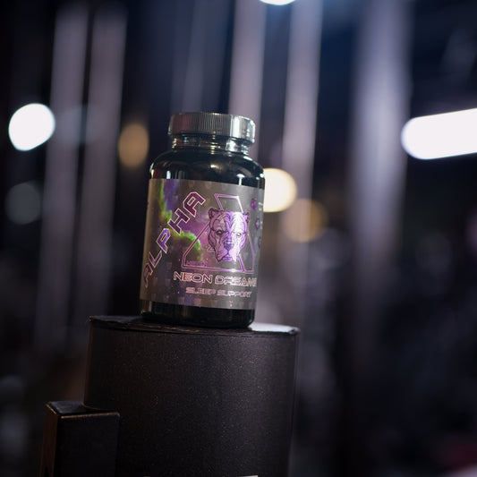 A small black supplement bottle with a metallic purple and pink label reading 'NEON DREAMS' sits on top of a black display stand in a dimly lit gym environment with blurred lights in the background.