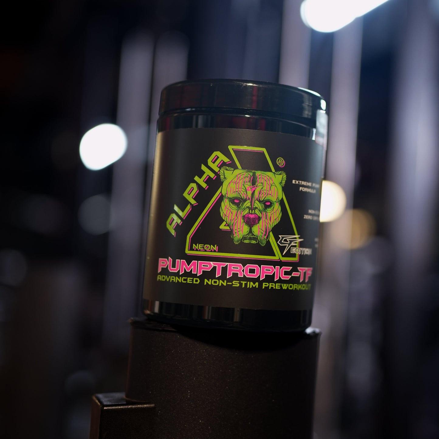 A black tub of Alpha Neon Pumptropic-tf pre-workout supplement with a colorful graphic label, set on a black gym equipment stand in a dark, blurred gym environment.