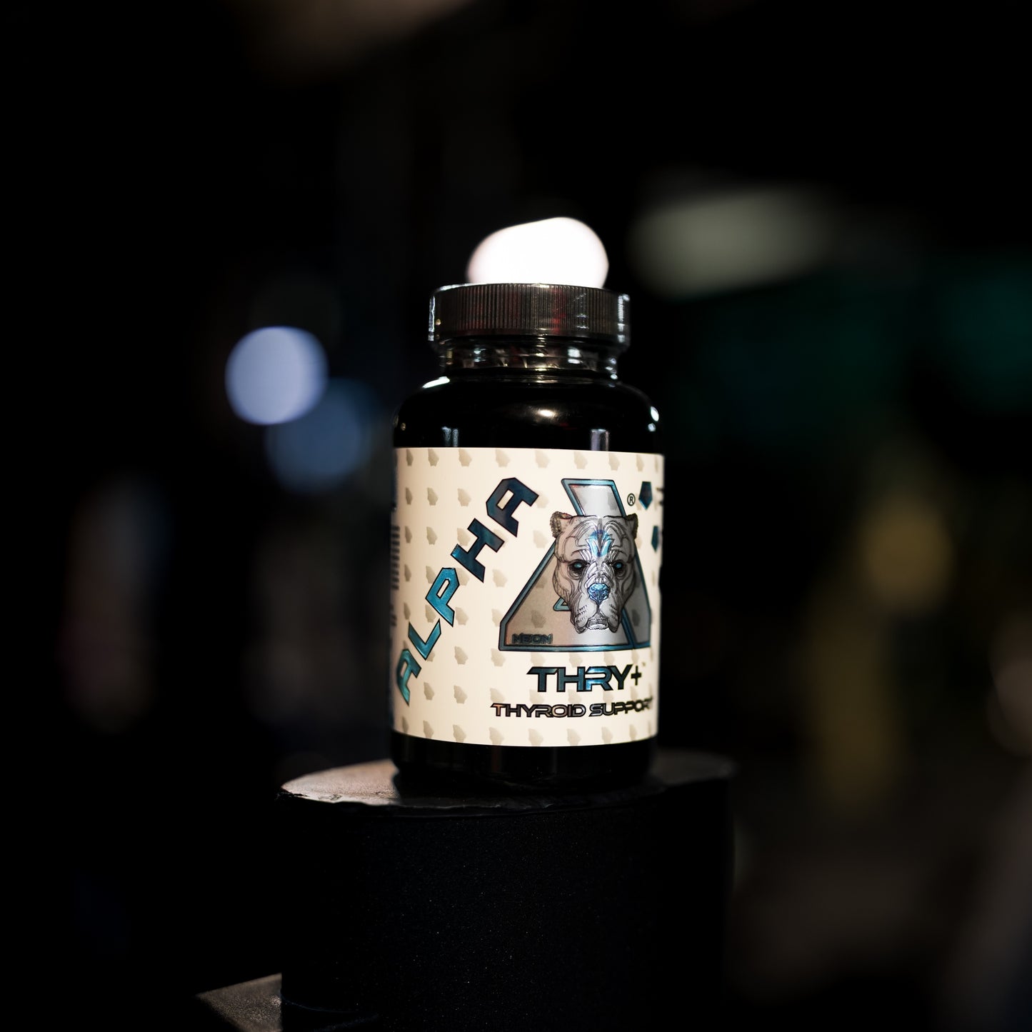 A bottle of Alpha Thry+ Thyroid supplement displayed on a black pedestal against a dark, blurred background.