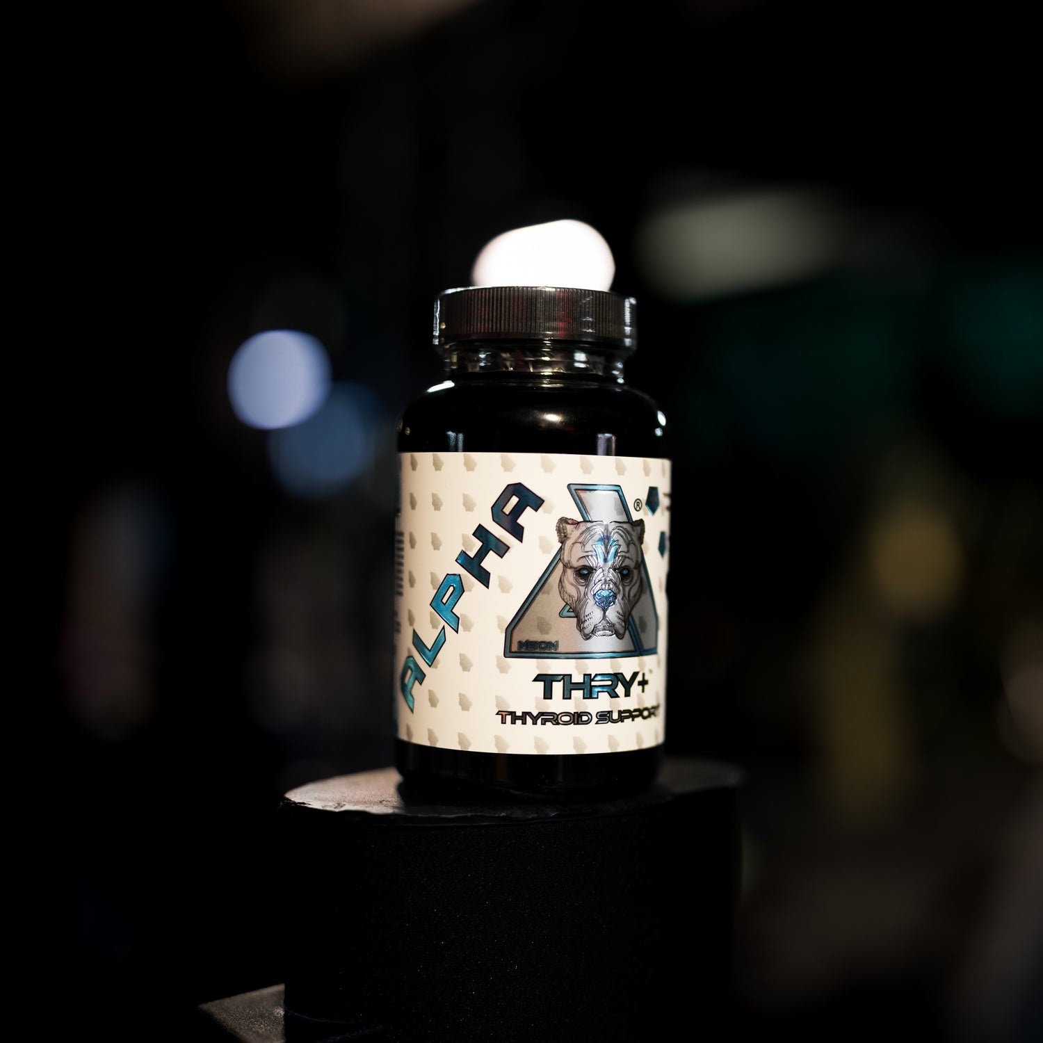 A bottle of Alpha Thry+ Thyroid supplement displayed on a black pedestal against a dark, blurred background.